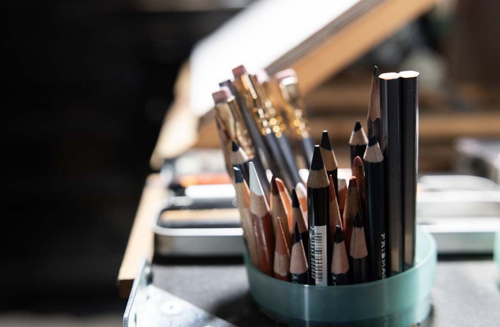 A cup of assorted drawing pencils beside drawing supplies