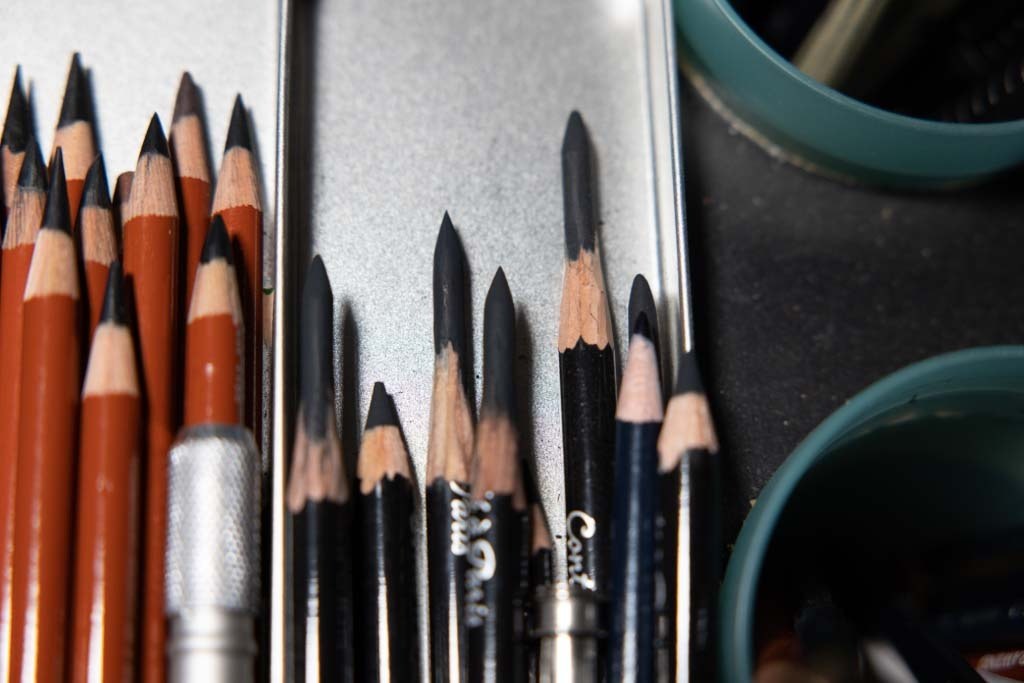 Close-up of sharpened drawing pencils arranged in a metal tray