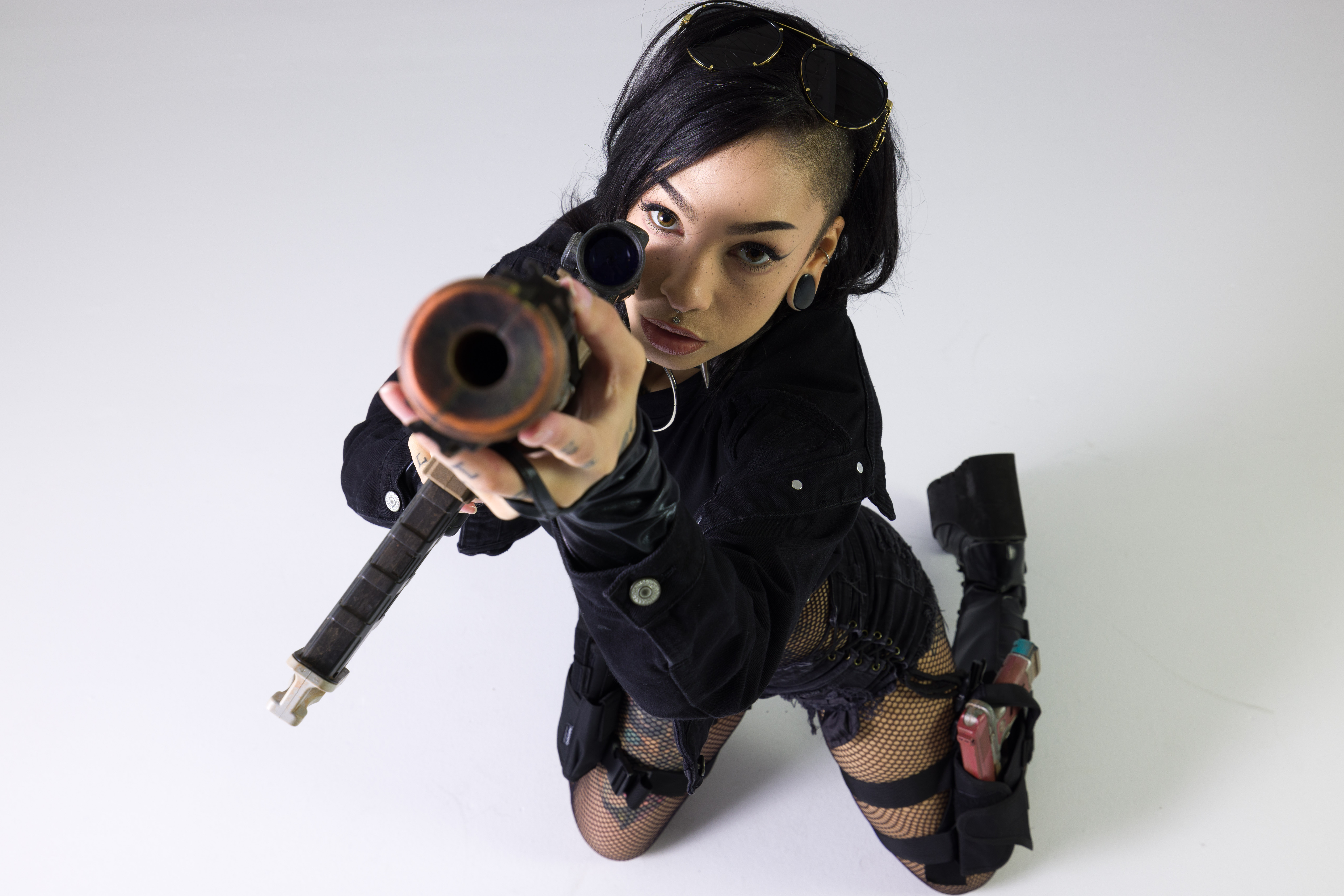Kneeling cyberpunk pose reference aiming a rifle prop toward the camera