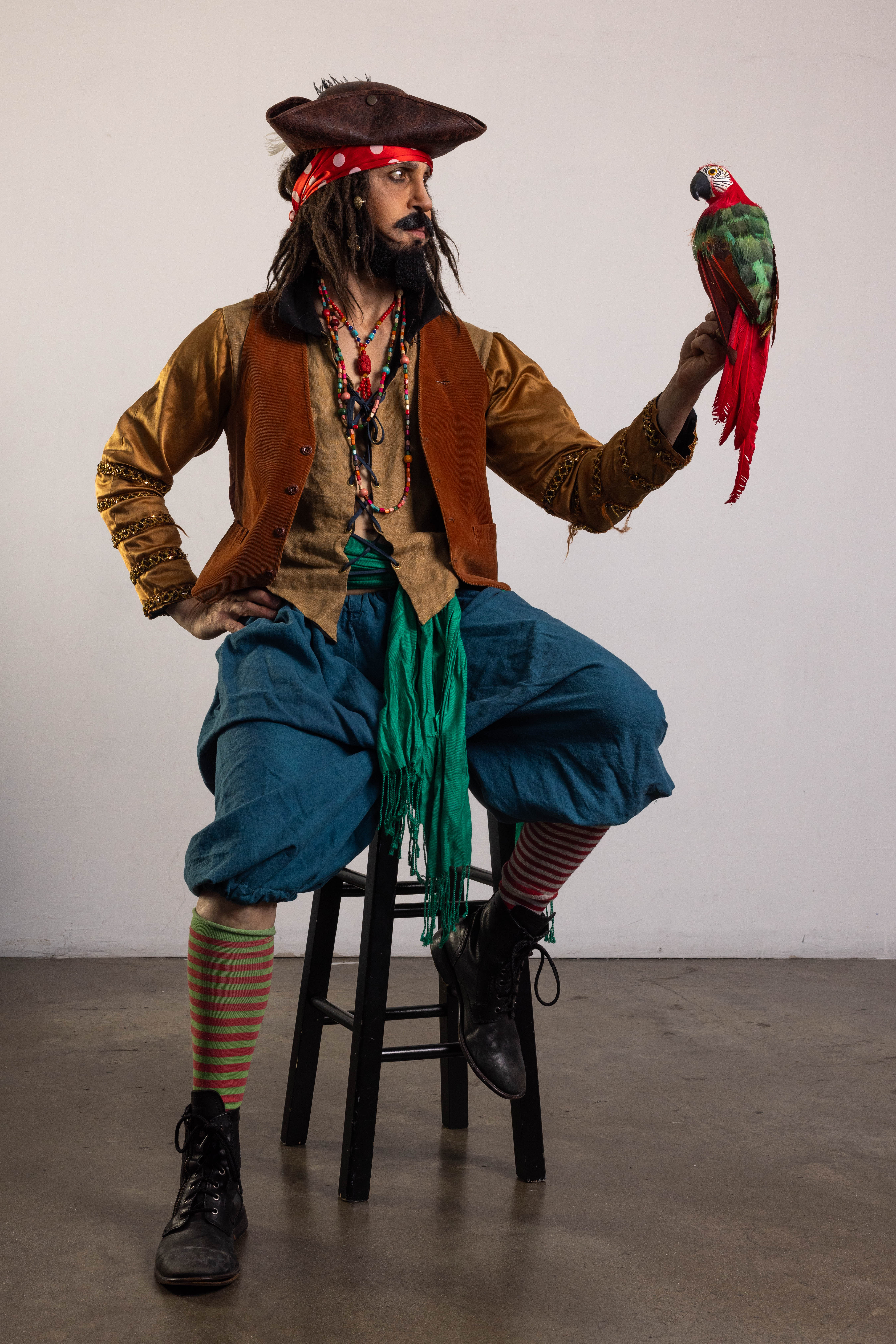 Seated pirate costume pose reference on a stool with an arm extended toward a parrot prop